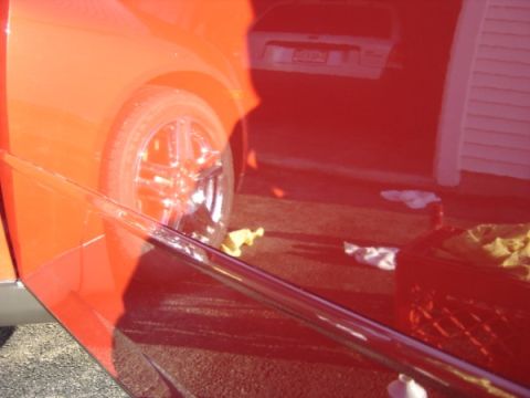 1999 Ford Taurus - Close-up of a red car's side panel and wheel, with reflections visible.