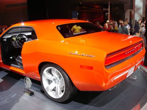 1986 Ford Bronco - An orange Dodge Challenger concept car is displayed with its door ajar, revealing the interior and a trophy at its base.