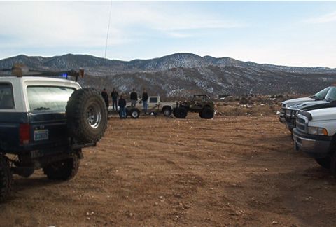 1986 Ford Bronco - A 1986 Ford Bronco is seen from the rear, with a spare tire on the back, parked in a dusty, outdoor setting with mountains in the backgroun…