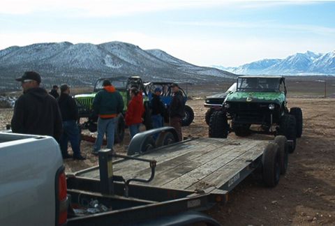 1986 Ford Bronco - Group of off-road vehicles and a trailer in a desert landscape with snow-capped mountains.