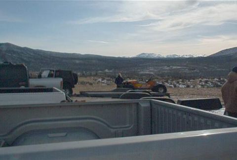 1986 Ford Bronco - Several vehicles are parked in a dry, open area with mountains in the distance under a cloudy sky.