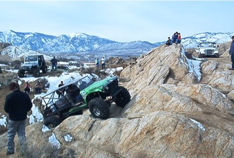 1986 Ford Bronco - Multiple off-road vehicles are seen climbing a rocky hill in a mountainous area.