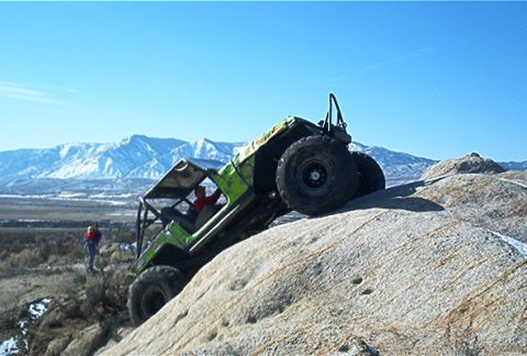 1986 Ford Bronco - Off-road vehicle navigates challenging rocky terrain with snow-capped mountains in the background.