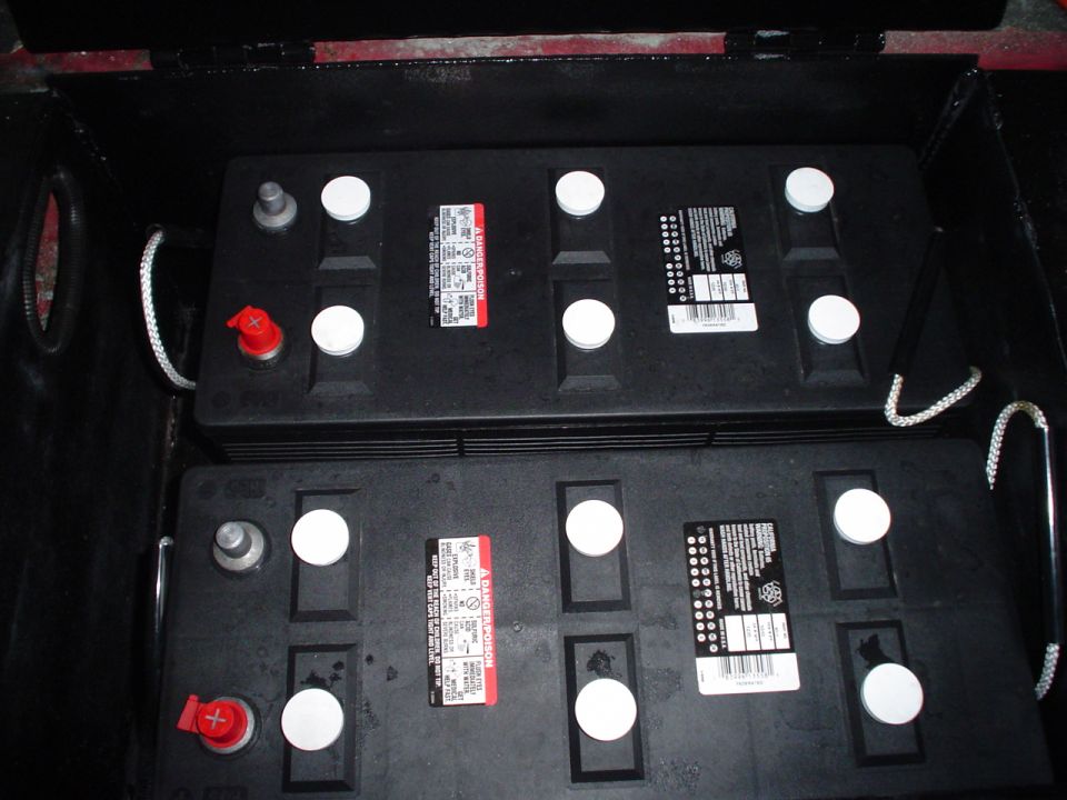 Two large black batteries with red and white caps in a compartment