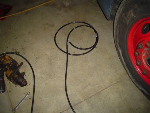 1966 International School Bus - A black hose and a drill are on the concrete floor near a vehicle's red wheel rim.