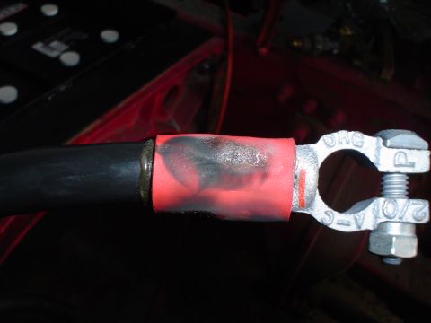 1966 International School Bus - A close-up shows a battery terminal clamp attached to a thick black cable, with red heat shrink tubing around the connection.