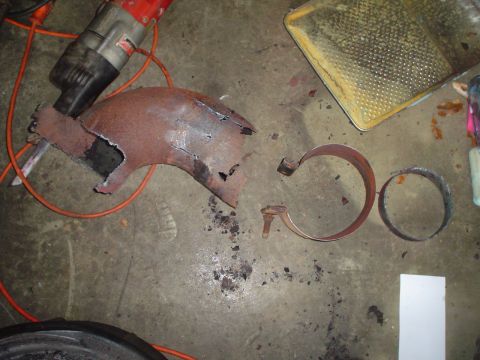 1966 International School Bus - Rusted exhaust pipe section and clamps lie on the floor near a drill, suggesting repair work.