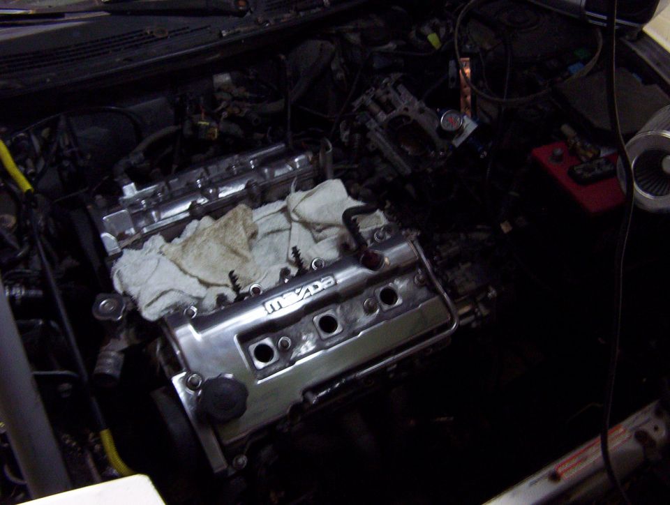 Engine bay with valve covers off a transverse Mazda V6 during a teardown, battery at right