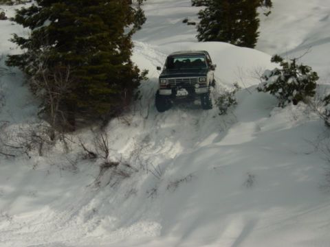 1986 Ford Bronco - A Ford Bronco navigates a snow-covered slope, leaving tire tracks behind.