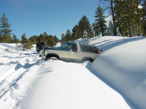 1986 Ford Bronco - A Ford Bronco navigates a snow-covered trail, with another vehicle visible behind it.