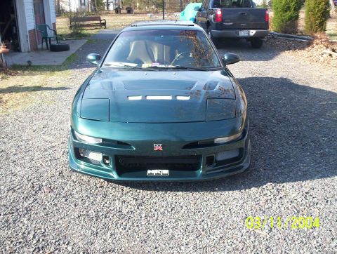 1997 Ford Probe - A green coupe with a modified front bumper and a Nissan GT-R emblem is parked on a gravel driveway. A pickup truck is visible in the backgr…
