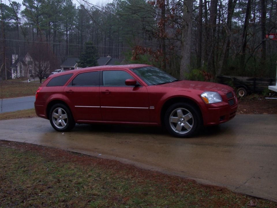 Red Dodge Magnum wagon on a wet driveway among pines, three-quarter front view