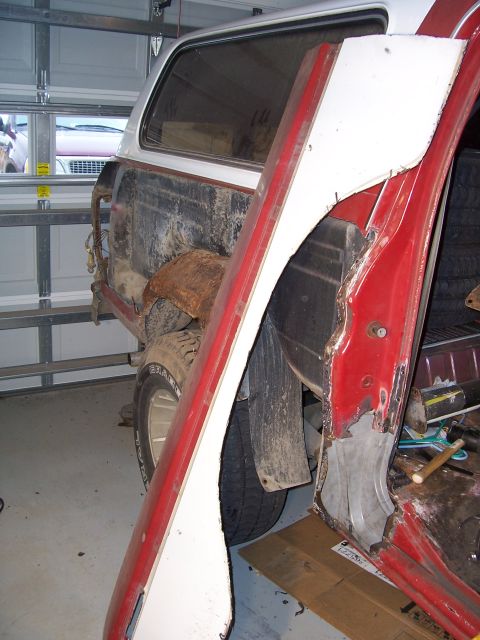 1978 Ford Bronco - Red-and-white SUV mid-teardown in a home garage, with the rear quarter panel and B-pillar area cut open to expose rusted inner structure an…