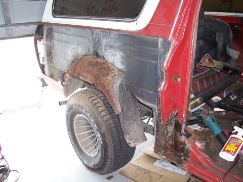 1978 Ford Bronco - Rear quarter of a red truck with the outer bedside skin cut away, exposing the rusty inner wheelhouse, bare inner panel and rotted rocker/B…