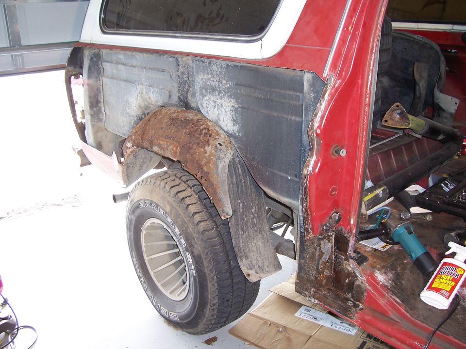 Red truck rear quarter cut open exposing rusty inner wheelhouse during rust repair