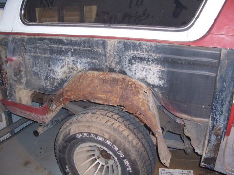 1978 Ford Bronco - Side view of a red-and-white SUV's rear quarter with the outer skin cut away, exposing a heavily rusted inner wheelhouse and stripped bare…