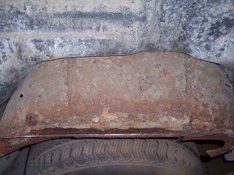 1978 Ford Bronco - The underside of a vehicle shows significant rust damage on a metal panel above a tire.