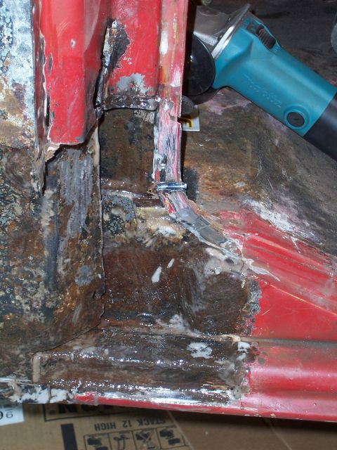 1978 Ford Bronco - Close-up of a rusted-out inner corner of a red body panel, with layers of scaly brown rust, old seam sealer and grinder marks exposing bare…
