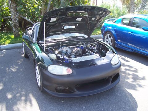 1994 Ford Probe - A green Mazda Miata is parked with its hood open, revealing the engine, next to a blue Mazda RX-8.