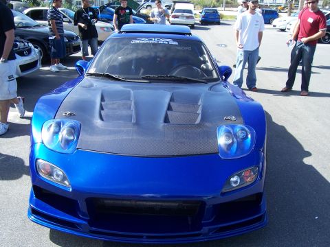 1994 Ford Probe - A modified blue Mazda RX-7 is parked at an outdoor car meet with several people observing.