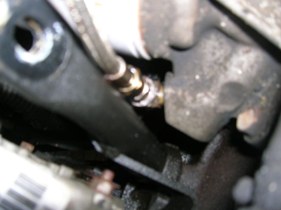 Close-up of a metal hose fitting on a dark engine component, showing some white residue