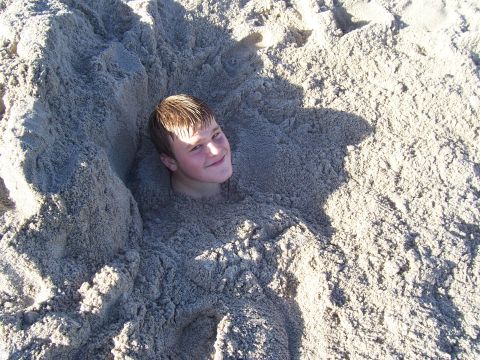 1994 Ford Probe - A person is buried in the sand on a beach, with only their head visible.
