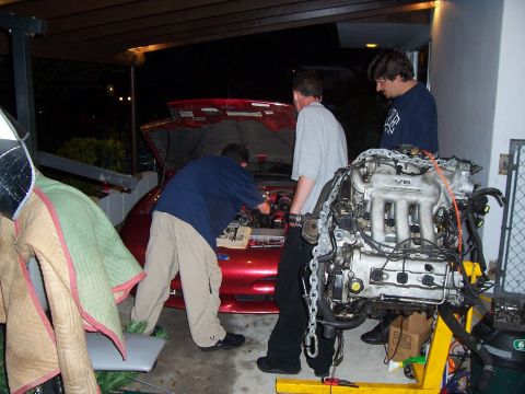 1994 Ford Probe - A V6 engine is being removed from a red car as three people work on the project.