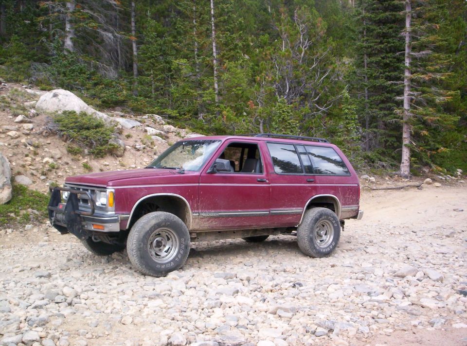 Maroon Chevy S-10 Blazer two-door lifted on a rocky alpine forest trail