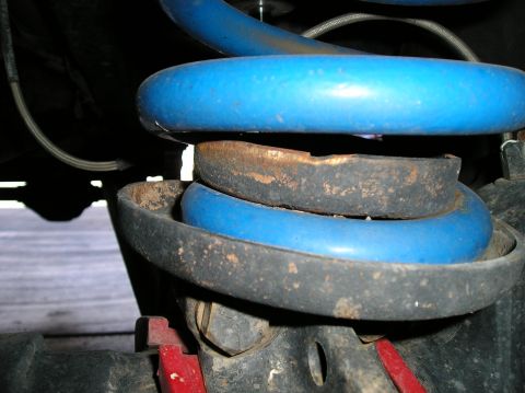 1993 Ford Bronco - This image shows a close-up of a vehicle's suspension system, focusing on a blue coil spring and its mounting hardware.
