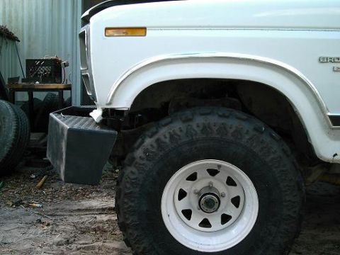 1986 Ford Bronco - Close-up of the front fender, bumper, and wheel of a white 1986 Ford Bronco.