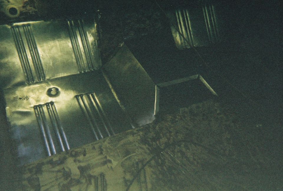Bare ribbed sheet metal floor pan panels installed in a vehicle floor during restoration, dark photo