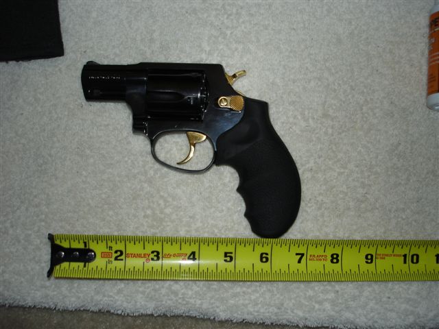 Black revolver with gold accents next to a yellow measuring tape