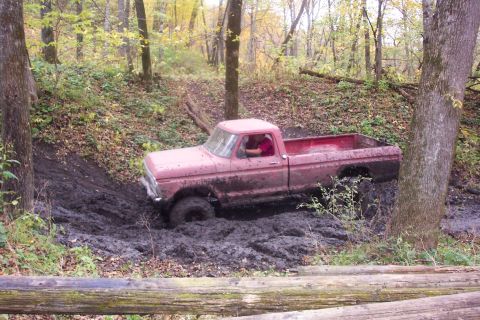 1973 Ford F-250 - A red 1973 Ford F-250 pickup truck is stuck in deep mud while driving off-road through a wooded area.