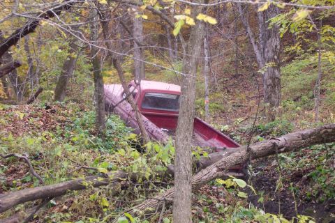1973 Ford F-250 - A red 1973 Ford F-250 pickup truck is seen off-road, surrounded by trees and undergrowth in a wooded area.