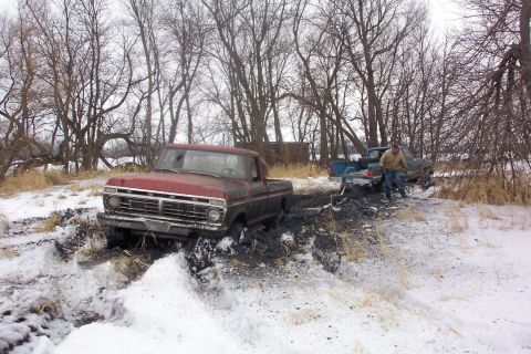1973 Ford F-250 - Two trucks are stuck in a muddy, snow-covered area with trees in the background.