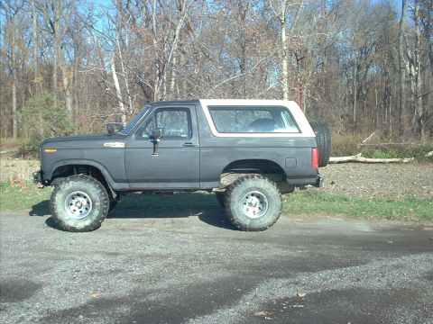 1986 Ford Bronco - This lifted Ford Bronco sits on a gravel surface with a wooded area in the background.
