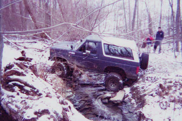 1986 Ford Bronco driving through a snowy stream