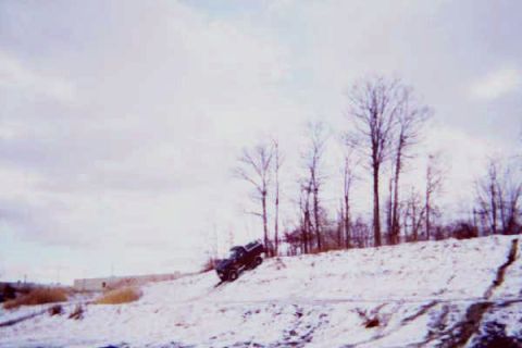 1986 Ford Bronco - A dark pickup truck navigates a snowy incline under a cloudy sky.