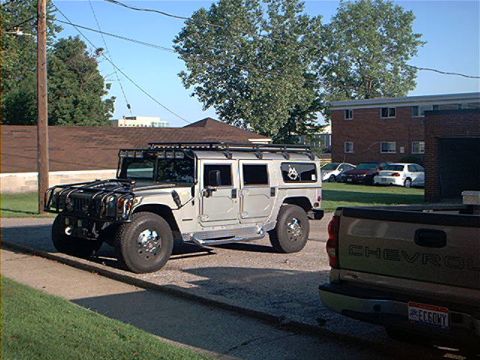 1986 Ford Bronco - A Hummer H1 is parked on the street next to a Chevrolet pickup truck.