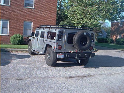 1986 Ford Bronco - A silver Hummer H1 is parked on an asphalt surface in front of a brick building.