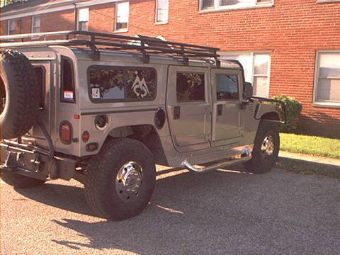 1986 Ford Bronco - This Hummer H1 features a roof rack and a spare tire mounted on the rear, seen from a three-quarter front perspective.