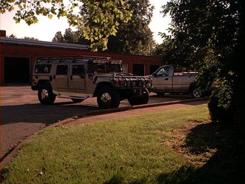 1986 Ford Bronco - Two vehicles, a Hummer H1 and a pickup truck, are parked outside a building.