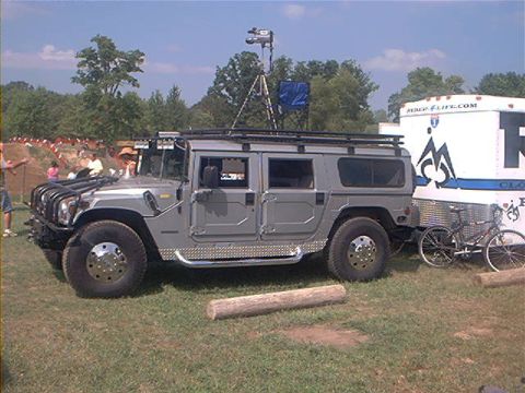 1986 Ford Bronco - A gray Hummer H1 is parked on grass next to a white trailer, with a bicycle nearby.