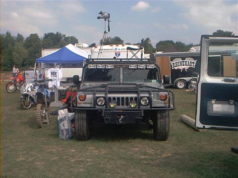 1986 Ford Bronco - Hummer H1 parked outdoors with camera equipment on roof; dirt bikes and trailers are visible.