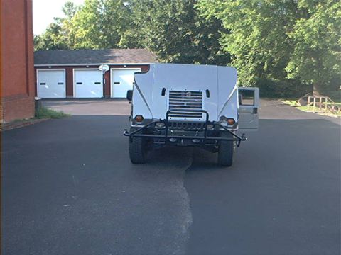 1986 Ford Bronco - The rear of a Humvee is shown parked in front of a three-bay garage with trees in the background.