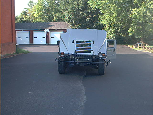Rear view of a light-colored Humvee parked in front of a garage