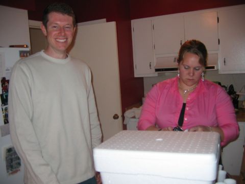 1985 Ford LTD Crown Victoria - A man and woman are in a kitchen, with the woman focused on a white box in the foreground.