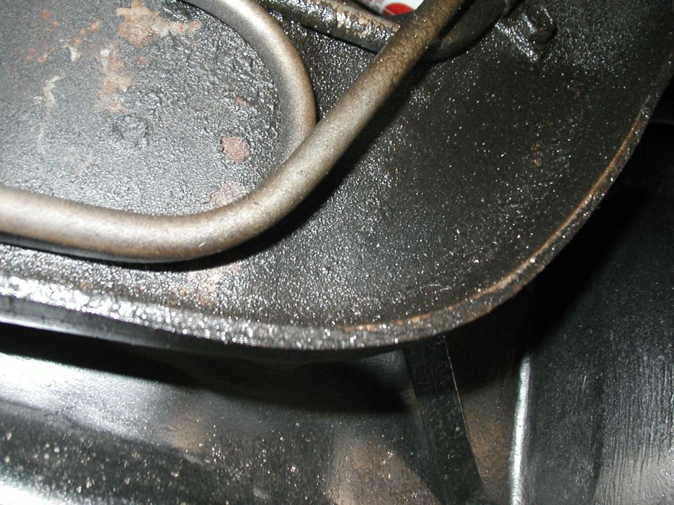 Close-up of black underbody metal with curved metal tube, surface rust and grime visible
