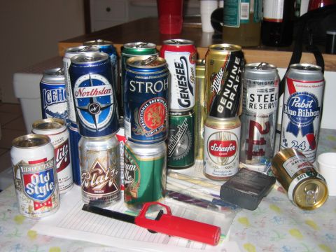 1985 Ford LTD Crown Victoria - A variety of beer cans are stacked and arranged on a table, alongside a red lighter and other miscellaneous items.