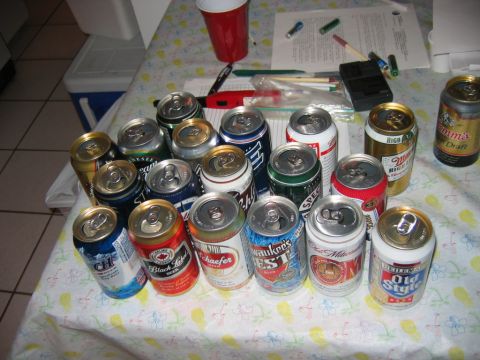 1985 Ford LTD Crown Victoria - A collection of various beer cans are spread across a table, accompanied by a red cup and writing materials.